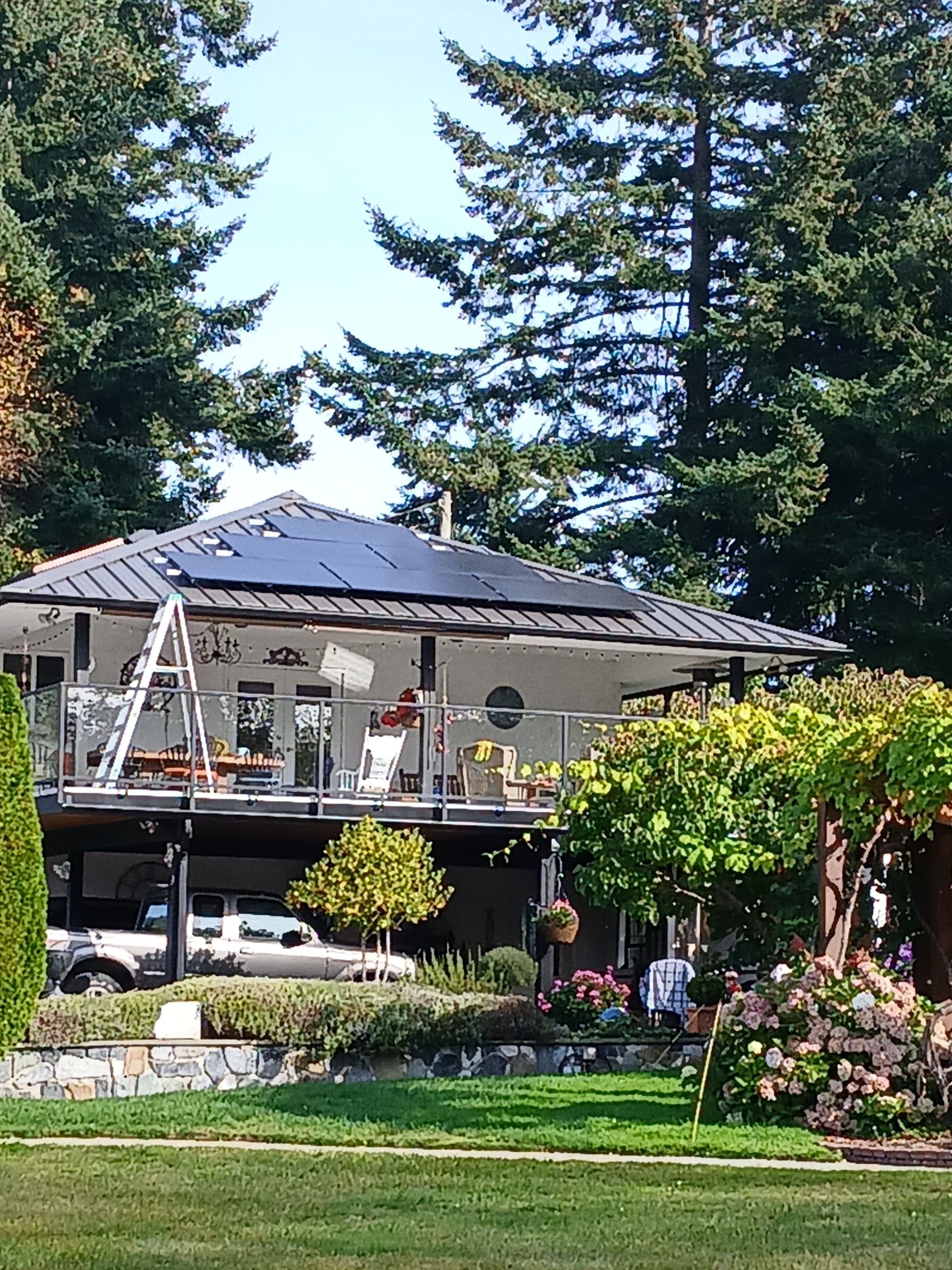 Rooftop solar array on a sloped residential roof, with forest behind the house.